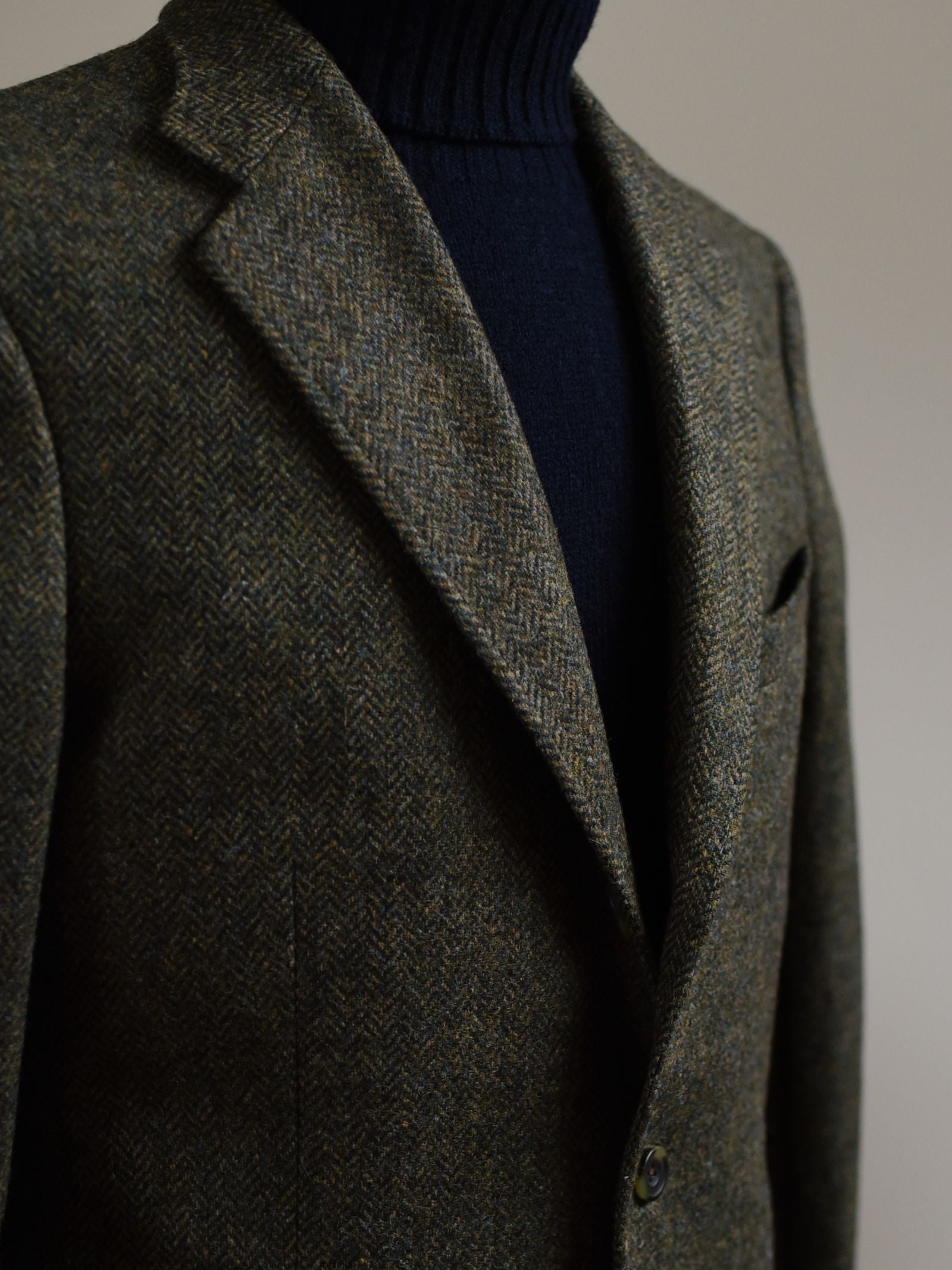 A close-up of a person wearing the Campbell's of Beauly Auld Stock Green Herringbone House Jacket over a dark navy turtleneck sweater, set against a neutral background.