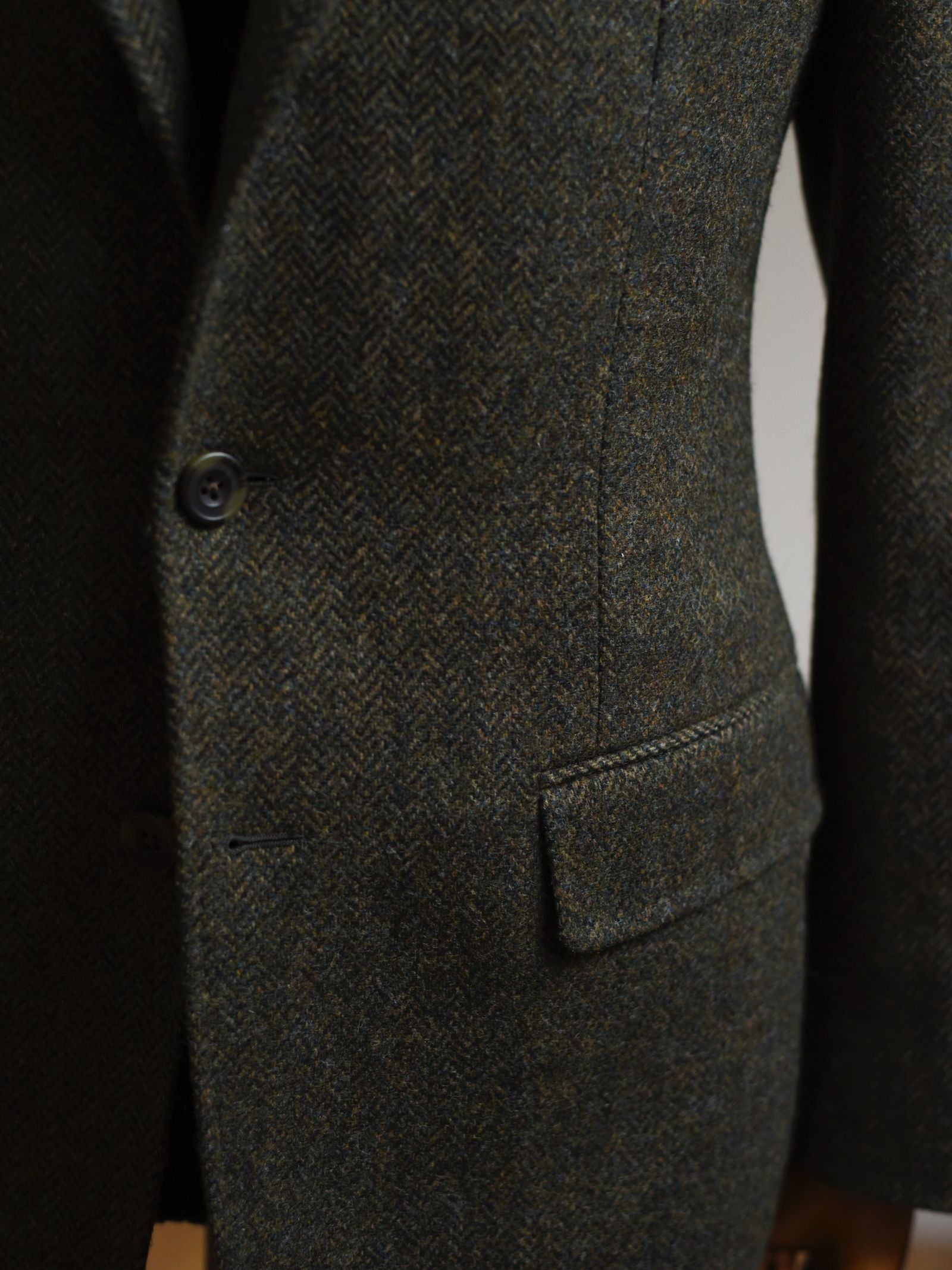 Close-up of the Auld Stock Green Herringbone House Jacket by Campbell's of Beauly, featuring two buttons, a flap pocket, and visible textured Shetland wool with tailored stitching.