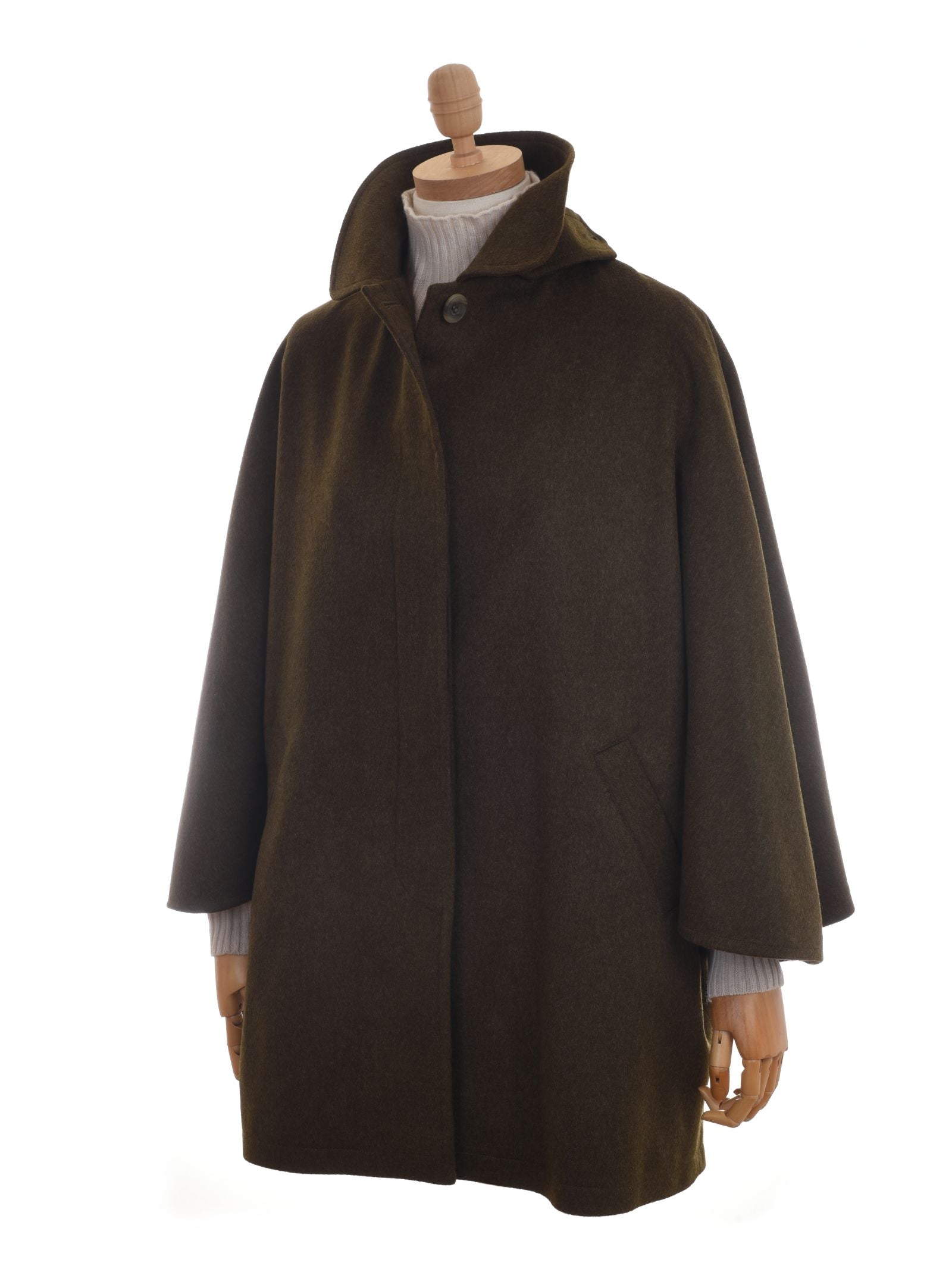 The Campbell's of Beauly Loden Green Cape features wide sleeves, a high collar, single top button, and two side pockets—shown over a white ribbed turtleneck. This heritage outerwear is crafted in dark olive green Austrian Loden.