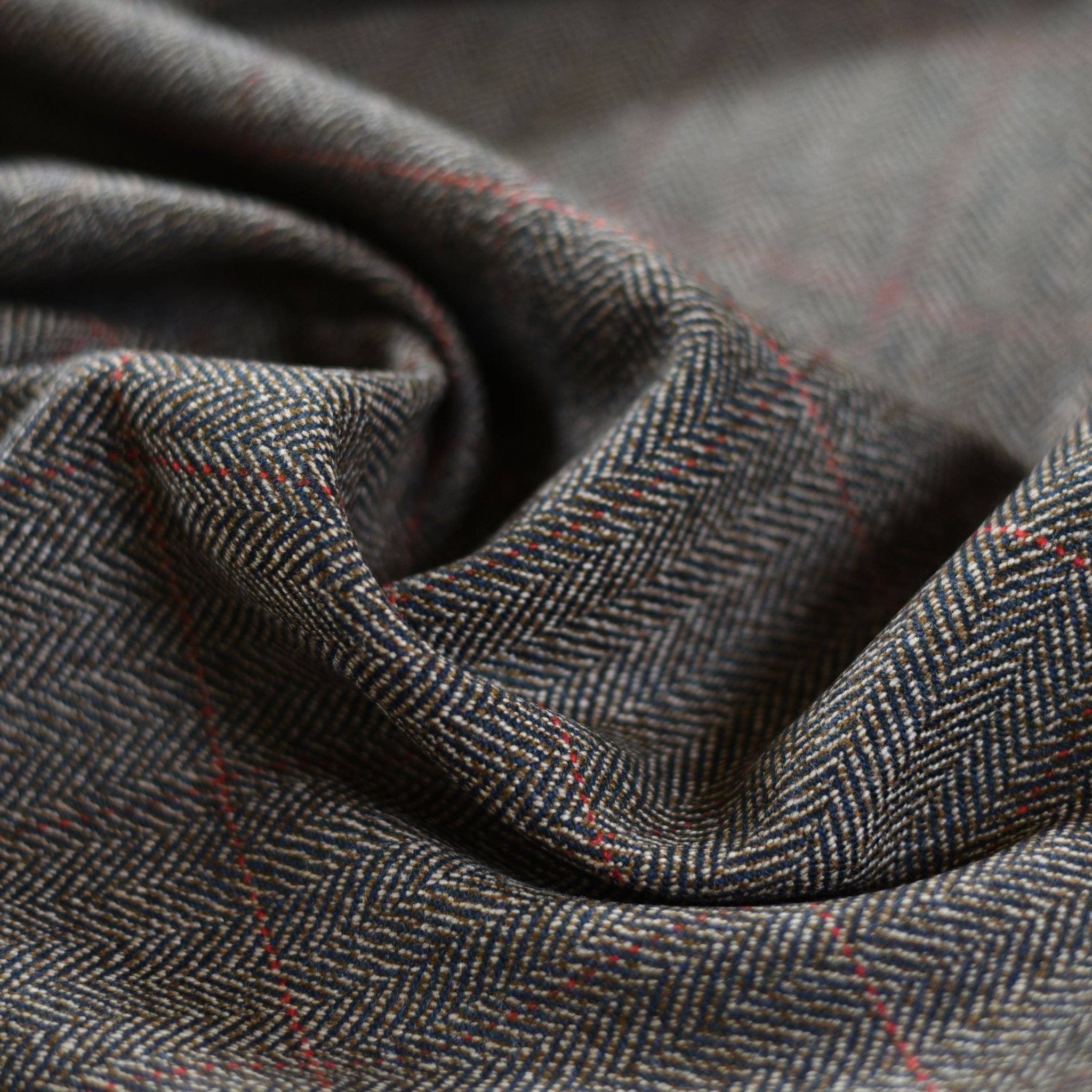 Close-up of Campbells of Beauly House Tweed 68866: lightweight herringbone fabric in gray with fine red lines, soft folds, and texture—showcasing timeless craftsmanship.
