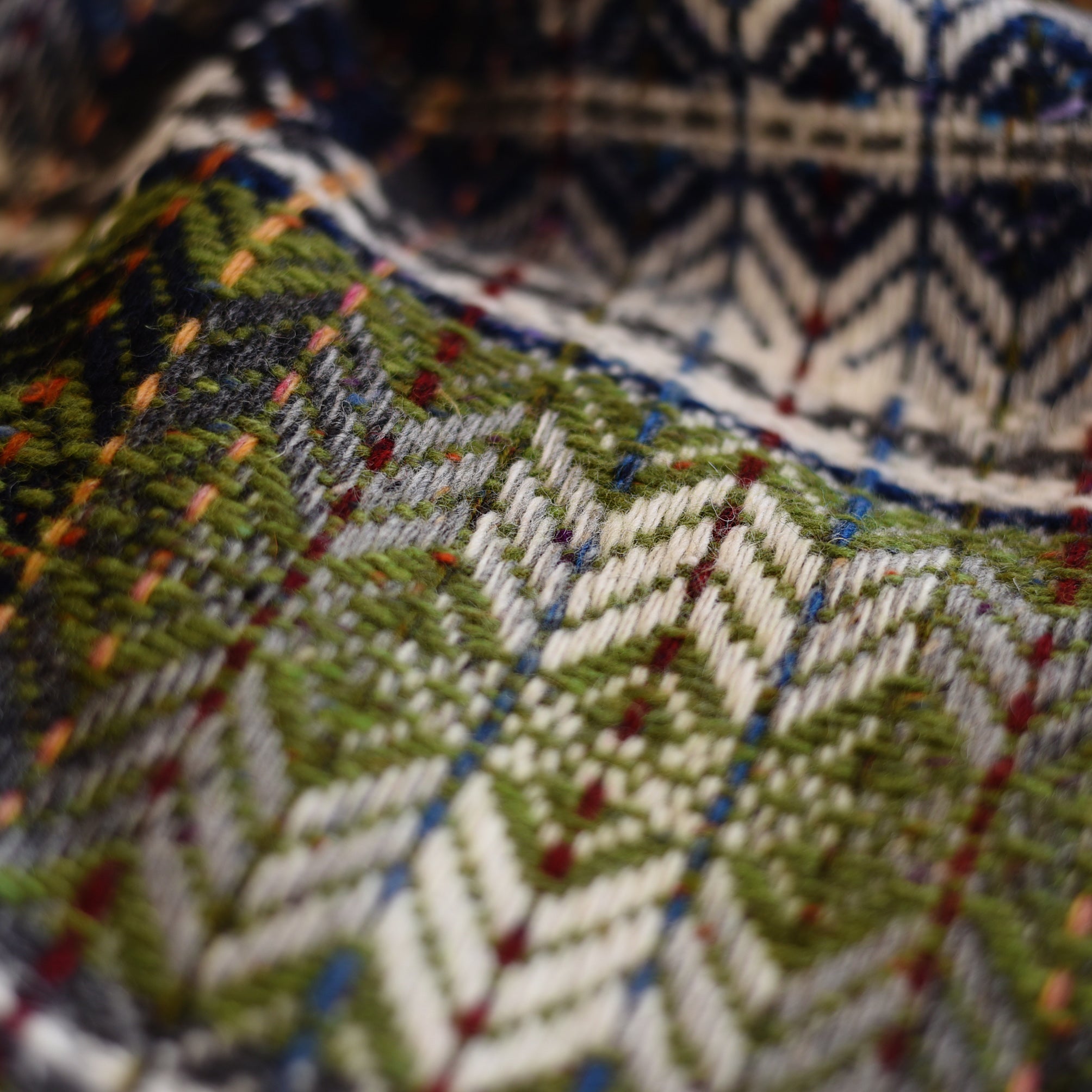 Close-up of the Wyvis Lambswool Throw by Campbells of Beauly, featuring colorful geometric patterns in green, white, yellow, blue, and red threads with a traditional diamond weave and detailed hand-crafted texture.