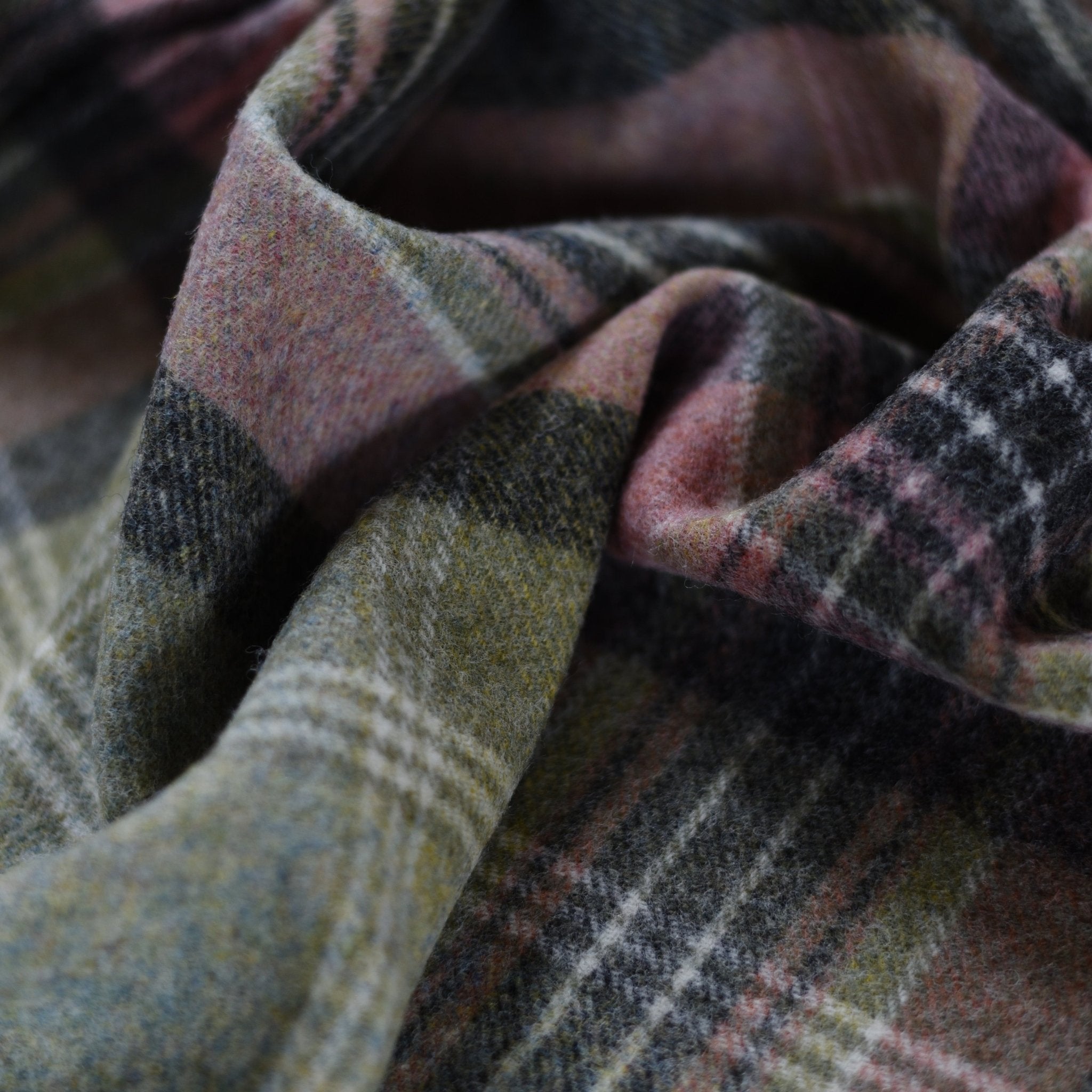 A close-up of the Inchmore Lambswool Throw by Campbells of Beauly, showcasing its soft, folded plaid fabric in green, pink, gray, and cream for a cosy touch.