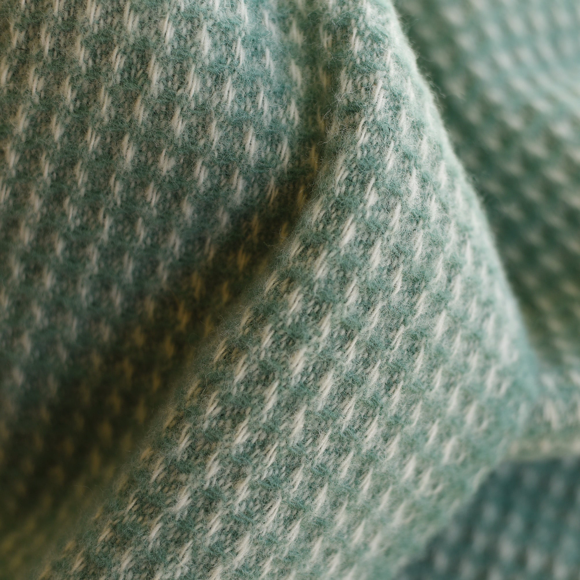 Close-up of the Campbells of Beauly Honeycomb Lambswool Throw, showcasing its soft, textured fabric in a green and white houndstooth pattern with visible honeycomb weave and gentle folds.