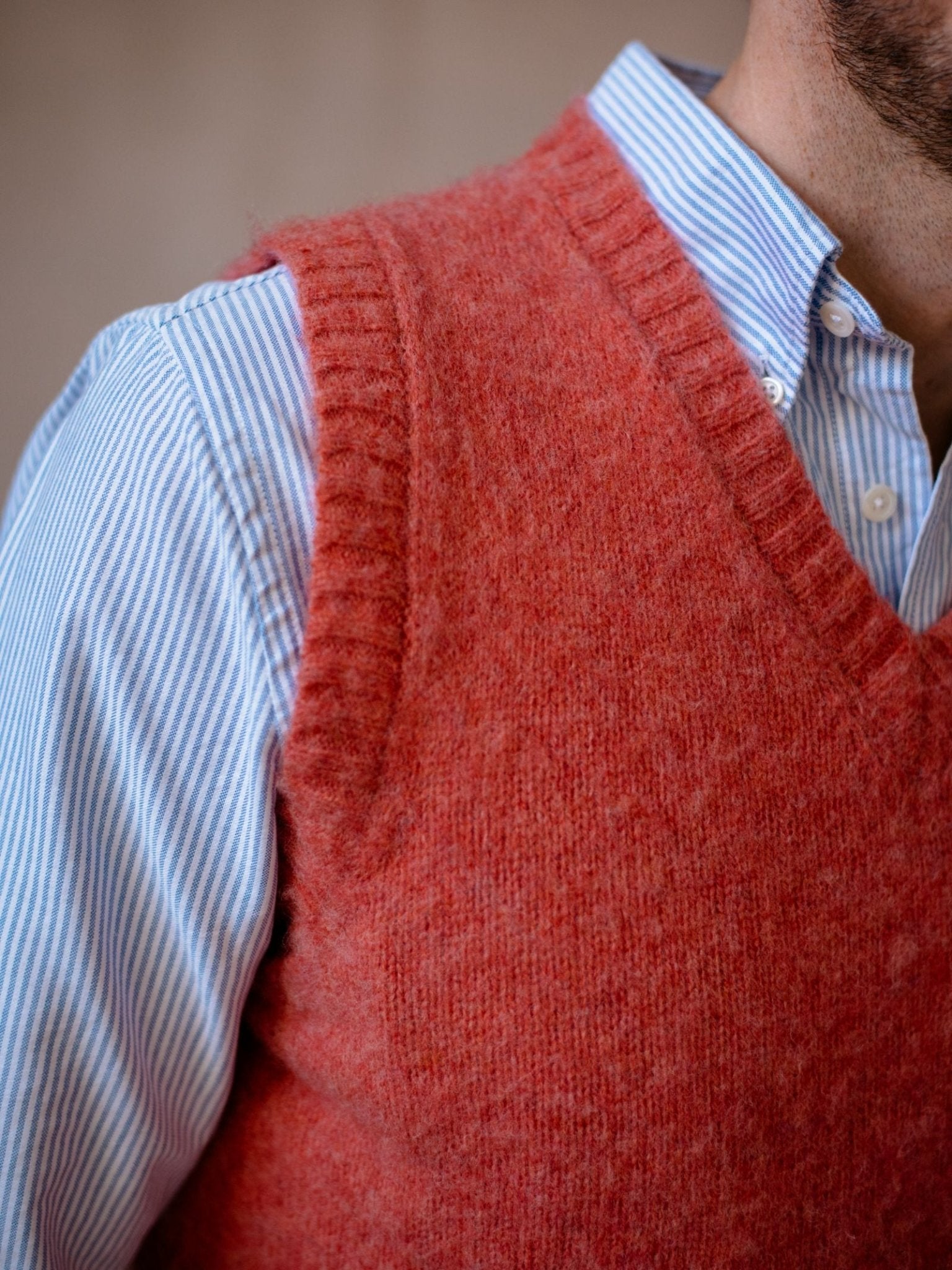 A person wears a light blue and white striped button-up shirt under a fuzzy, red Campbell's of Beauly Auld Stock Shetland Slipover V-neck knit. Only the upper torso and part of the neck are visible.