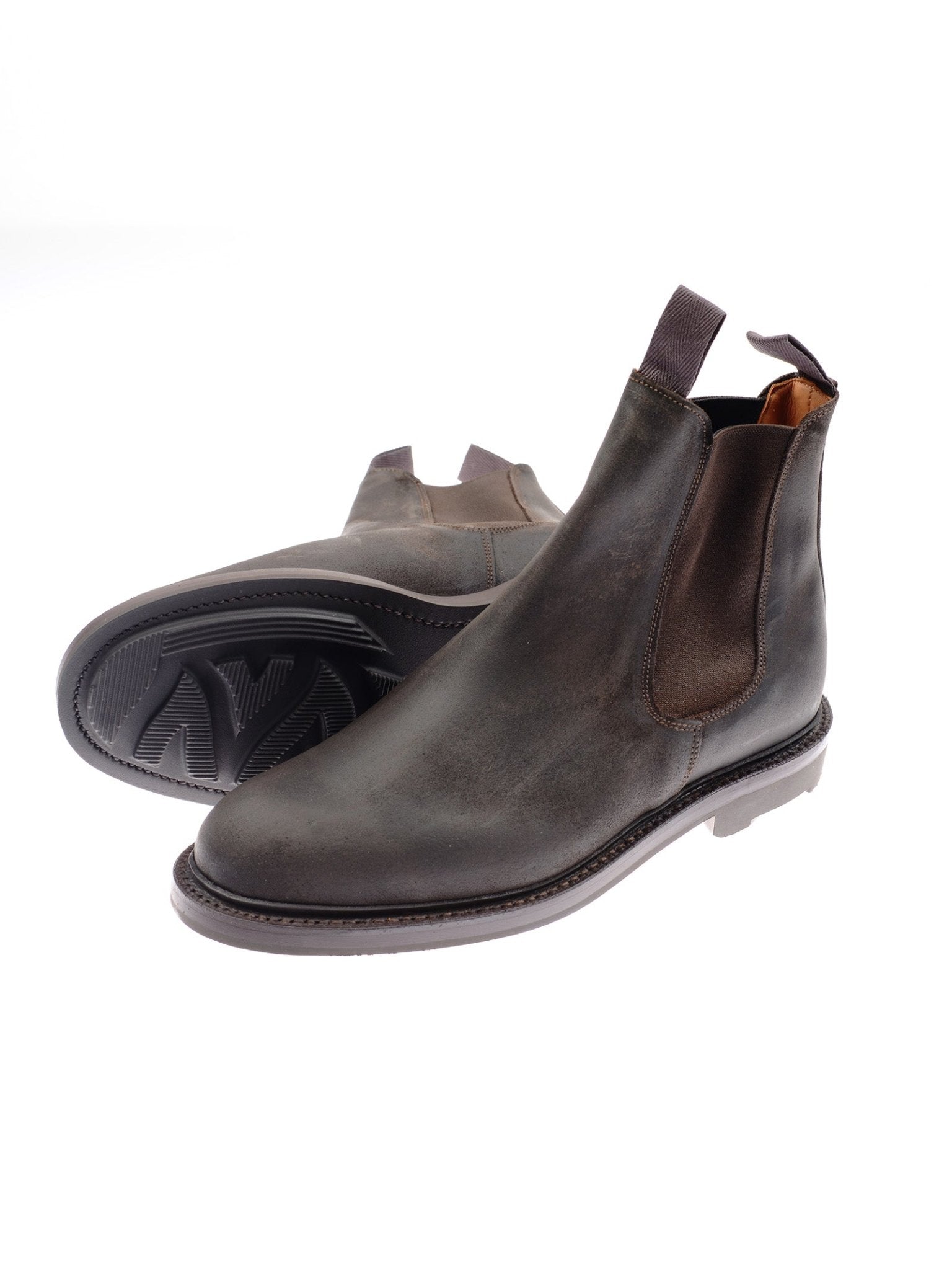 The Lowlander Boots by Campbell's of Beauly are dark brown leather Chelsea boots, handmade in England with water-resistant suede, elastic side panels, pull tabs, and a treaded sole. One boot stands upright while the other shows the sole.
