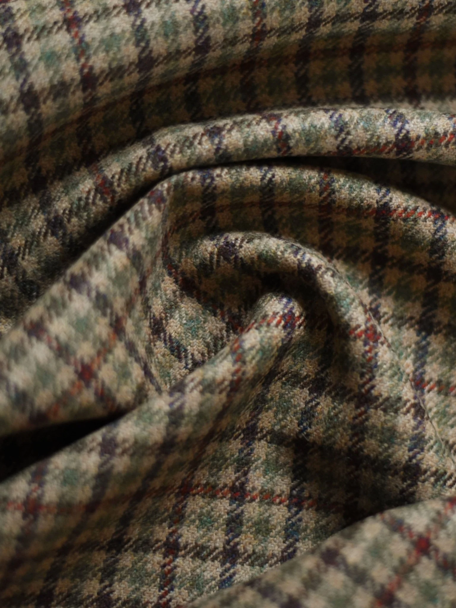 Close-up of folded wool fabric with a green, brown, and red plaid pattern, showing soft texture and gentle creases.