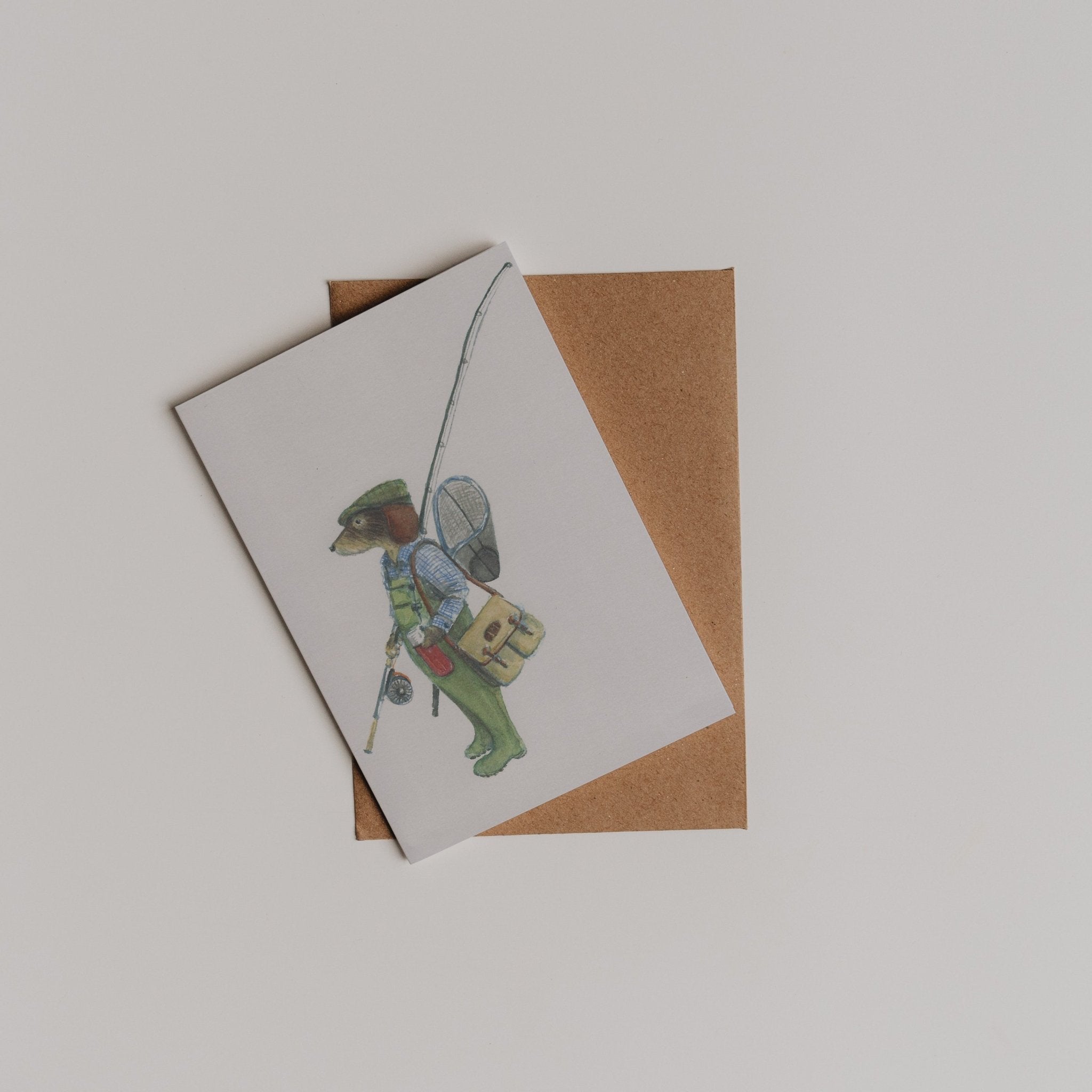 The Fishing Dachshund Greeting Card by Campbells of Beauly, illustrated by Sophie Murray, shows a dachshund dressed as a fisherman and comes with a brown envelope displayed on a white surface.