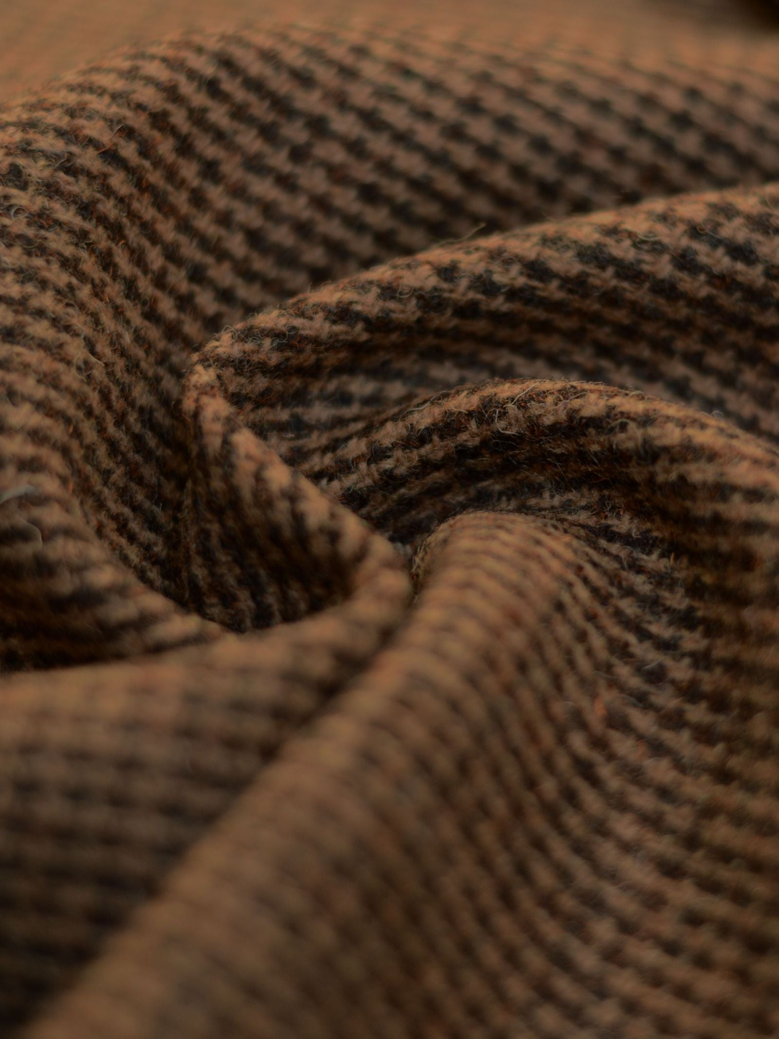 Close-up of Harris Tweed 93905 by Campbell's of Beauly, showcasing brown and black houndstooth folds and textured fibers—a tribute to classic Scottish weaving that evokes warmth and coziness.
