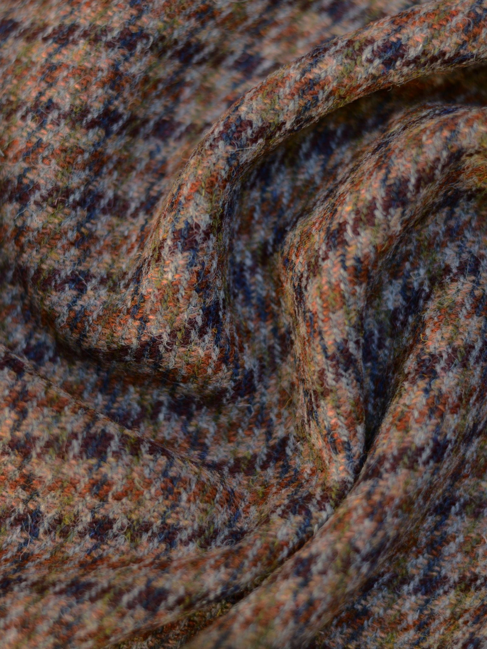 Close-up of Campbell’s of Beauly Harris Tweed 93914 fabric, showcasing a houndstooth pattern in muted brown, orange, green, and navy blue tones. Gentle folds and soft light highlight its unique woven texture.