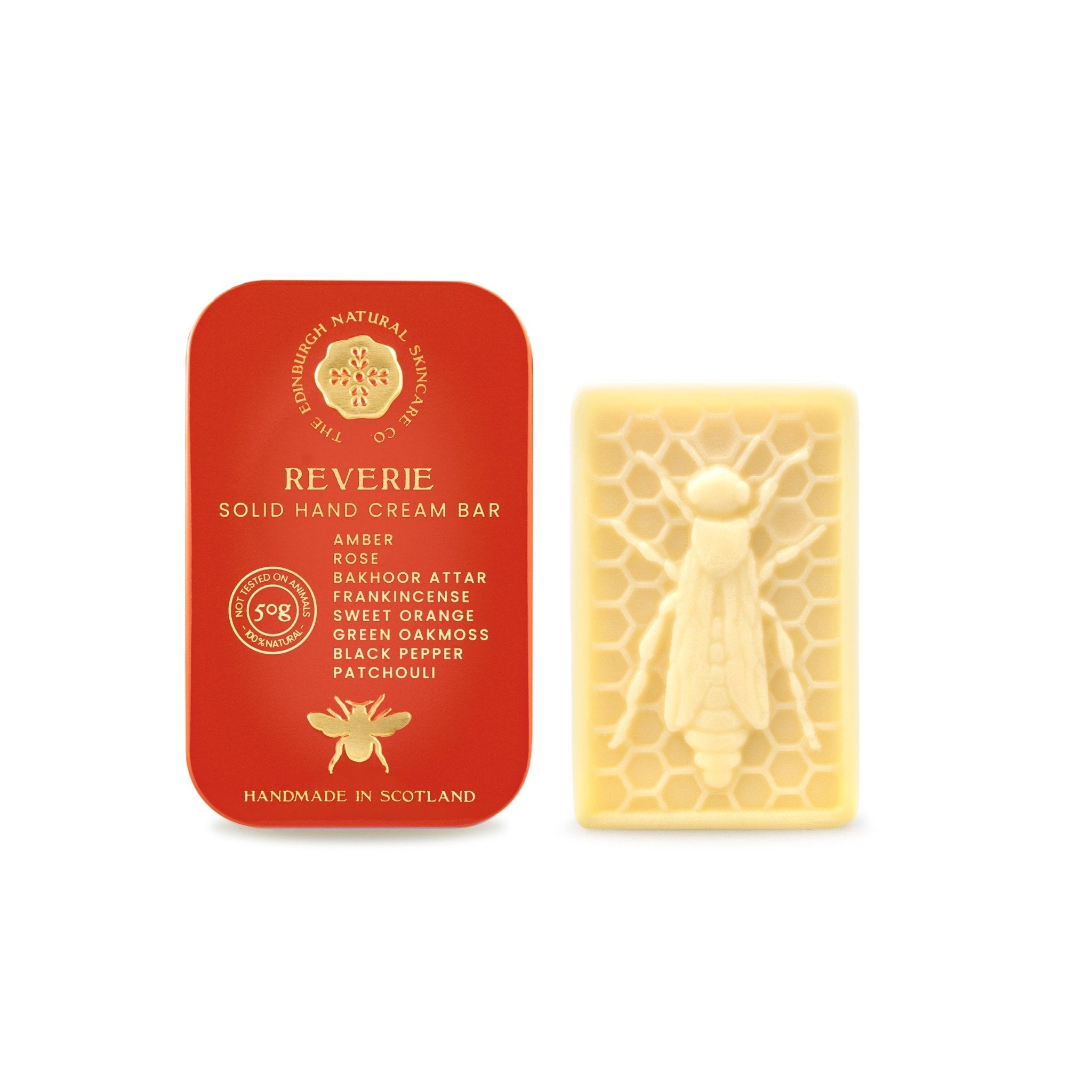 A red tin labeled Reverie Hand Cream Bar by The Edinburgh Natural Skincare Company sits beside a cream-colored hand cream bar with a bee and honeycomb design, displaying its list of scents.