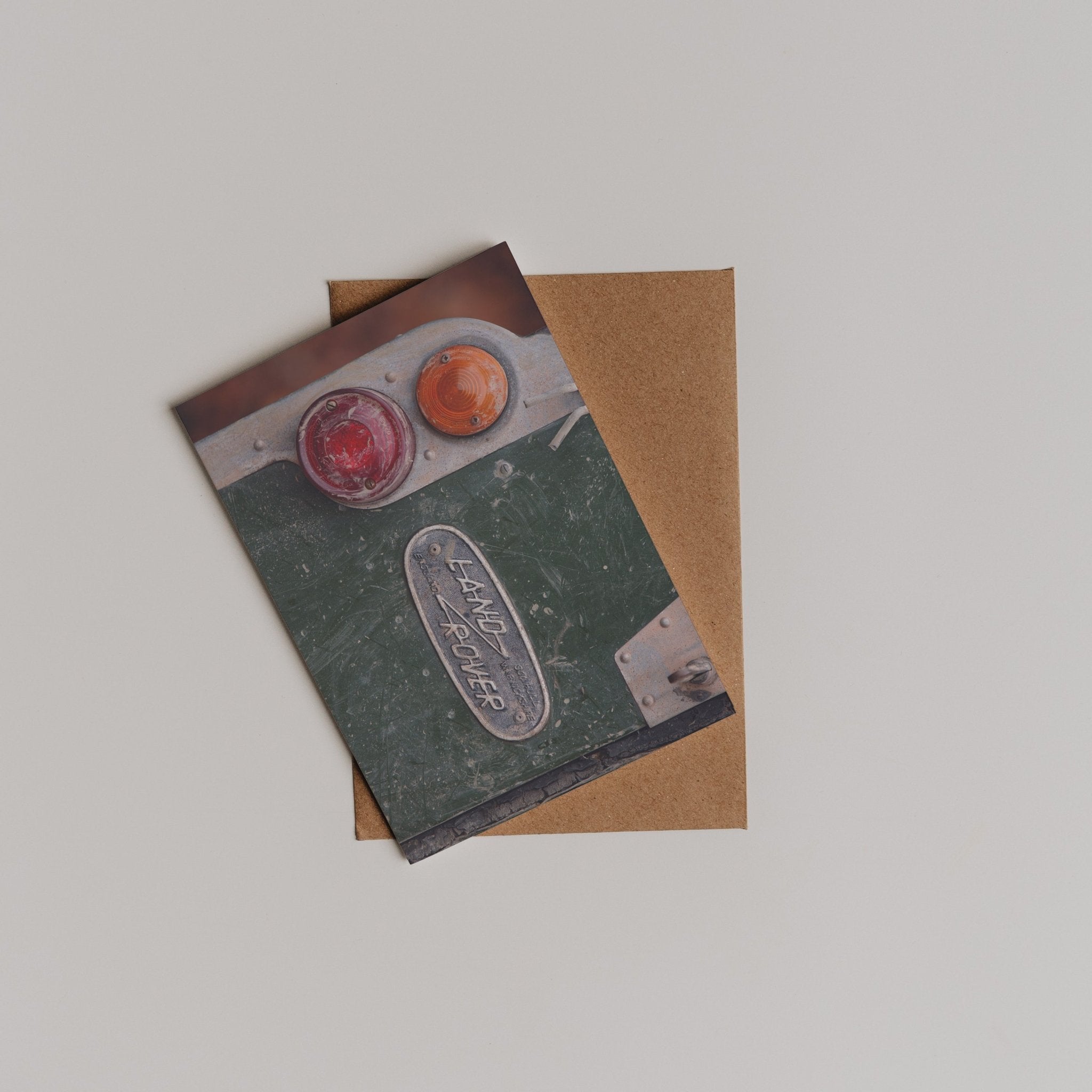 The Land Rover Defender Greeting Card by Campbell's of Beauly features a classic Land Rover tail light and badge on the front and comes with a brown envelope, both displayed on a light surface.