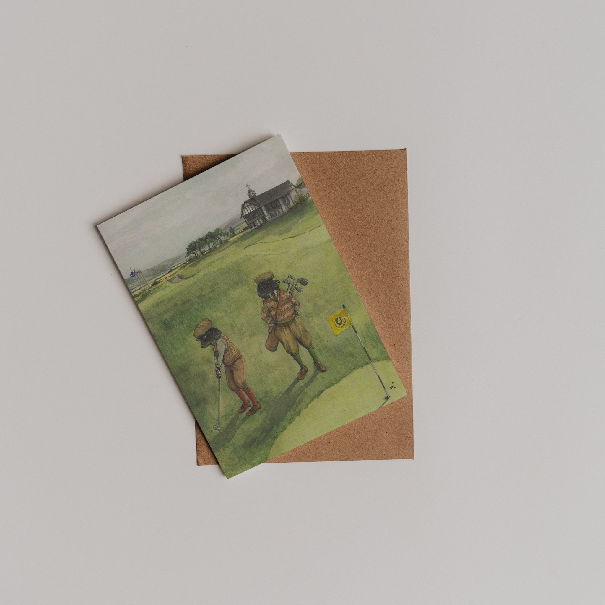 The Links Dornoch Greeting Card from Campbell's of Beauly features two golfers on a green field, designed by Sophie Murray, and is shown atop a brown envelope against a white background.