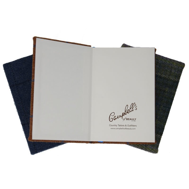 An open Campbell's of Beauly Tweed Notebook with A5 plain paper—blank left page, branded right page—rests atop two closed, fabric-covered sustainable Tweed Notebooks.