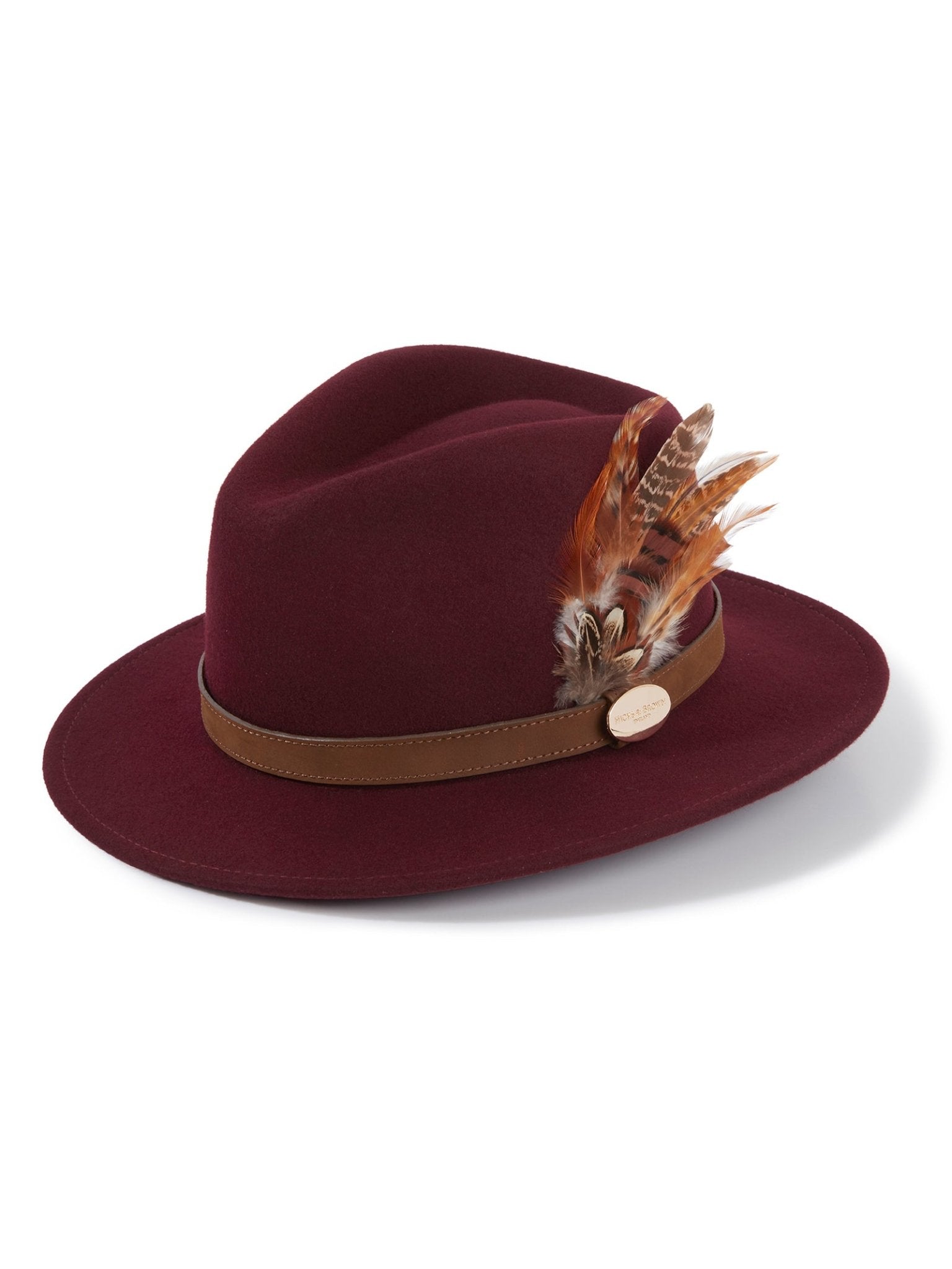 The Hicks & Brown Auld Stock Gamebird Fedora is a burgundy wool felt hat with a brown leather band, gold button, and a feather wrap featuring clustered brown and beige feathers on the side.