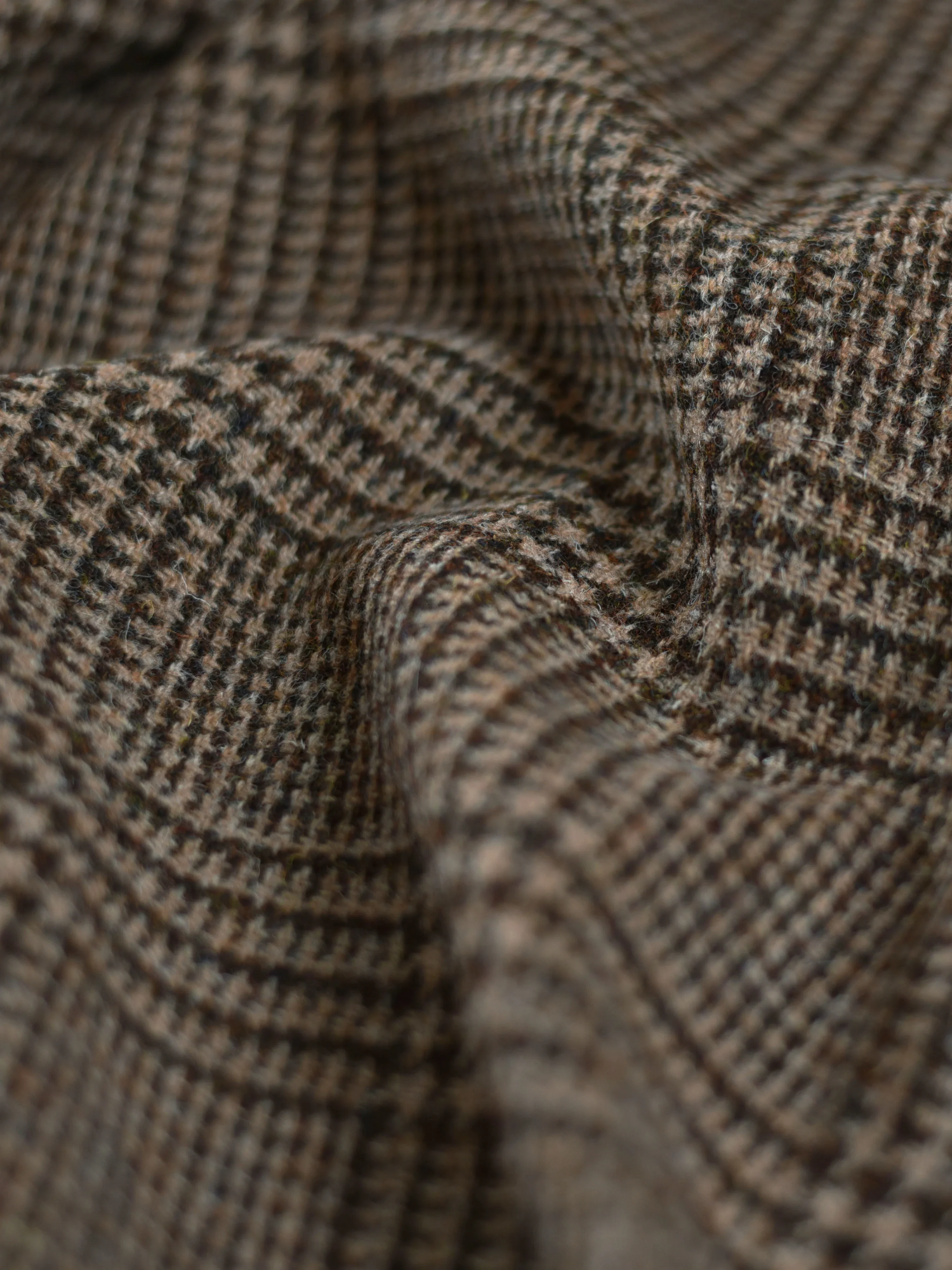 Close-up of brown and beige houndstooth patterned fabric with visible texture and folds, highlighting the woven material and intricate checkered design.