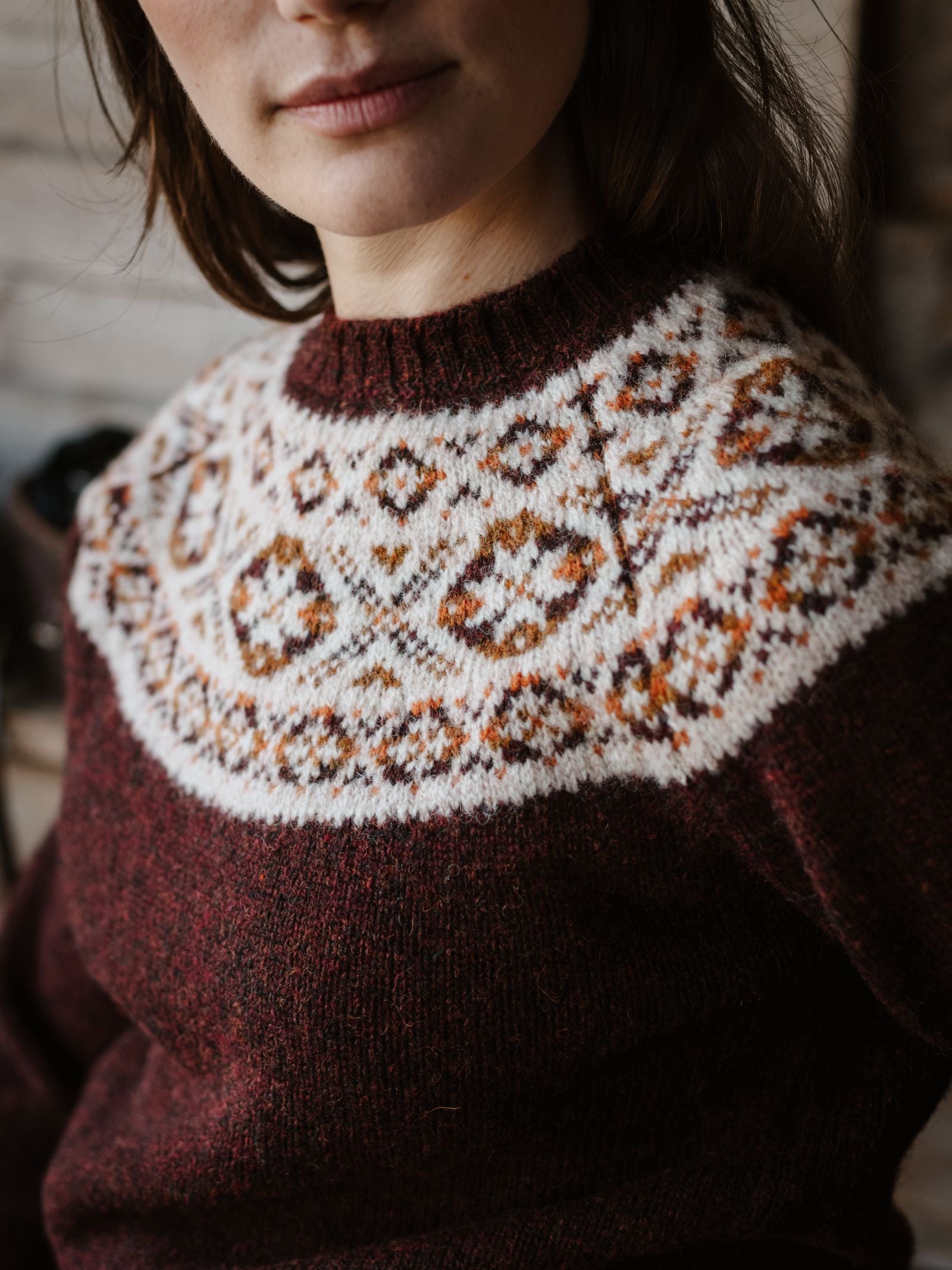 A woman wearing the Campbell's of Beauly Shetland Fairisle Crew—a maroon traditional crew neck sweater with a white, brown, and orange Fair Isle yoke. The image is cropped to show her from the shoulders up.