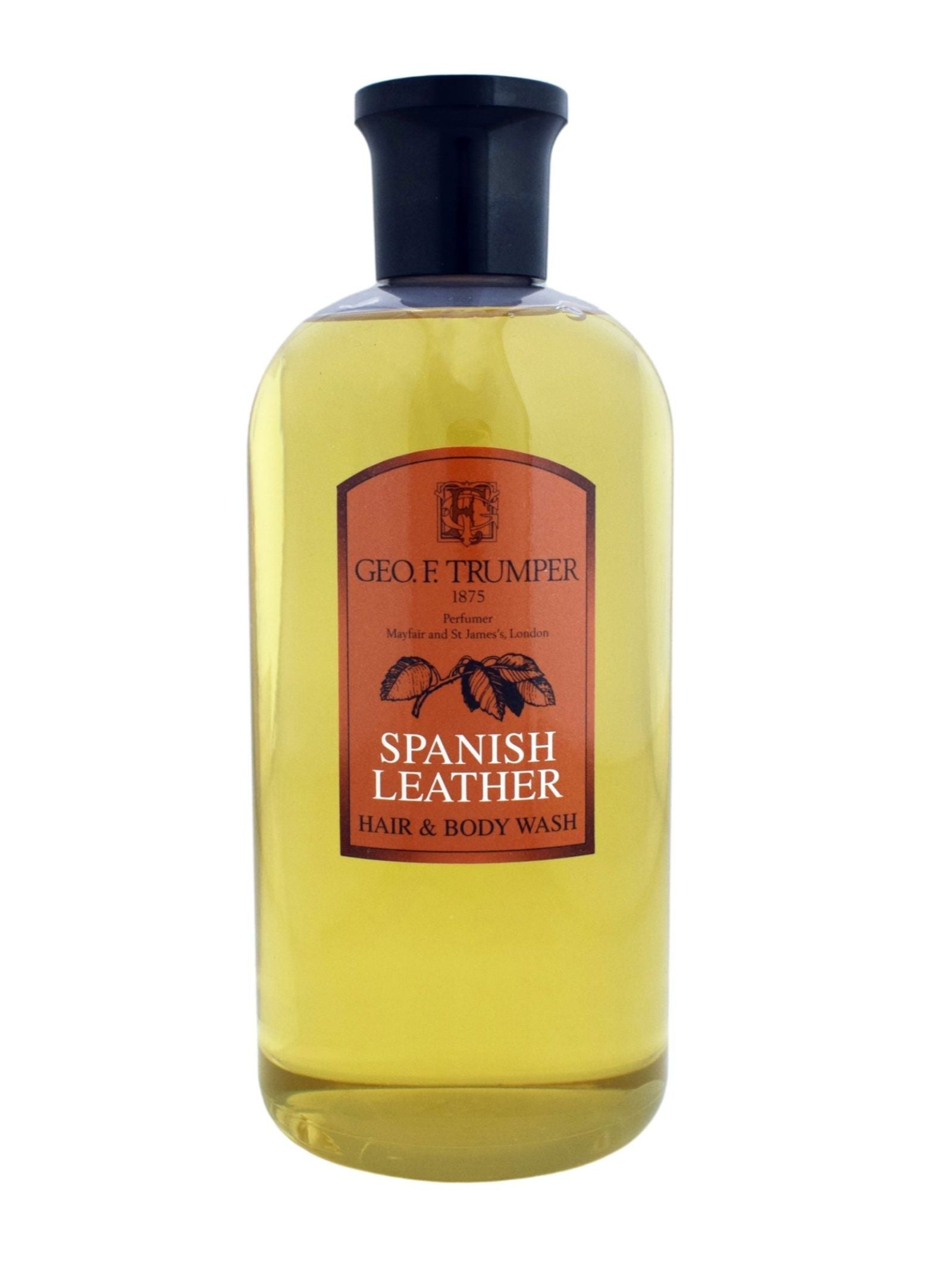 A clear bottle of Geo. F. Trumper Hair & Body Wash features a black cap and amber label, displaying the brand and product name, while the light amber liquid inside suggests luxurious sandalwood notes.