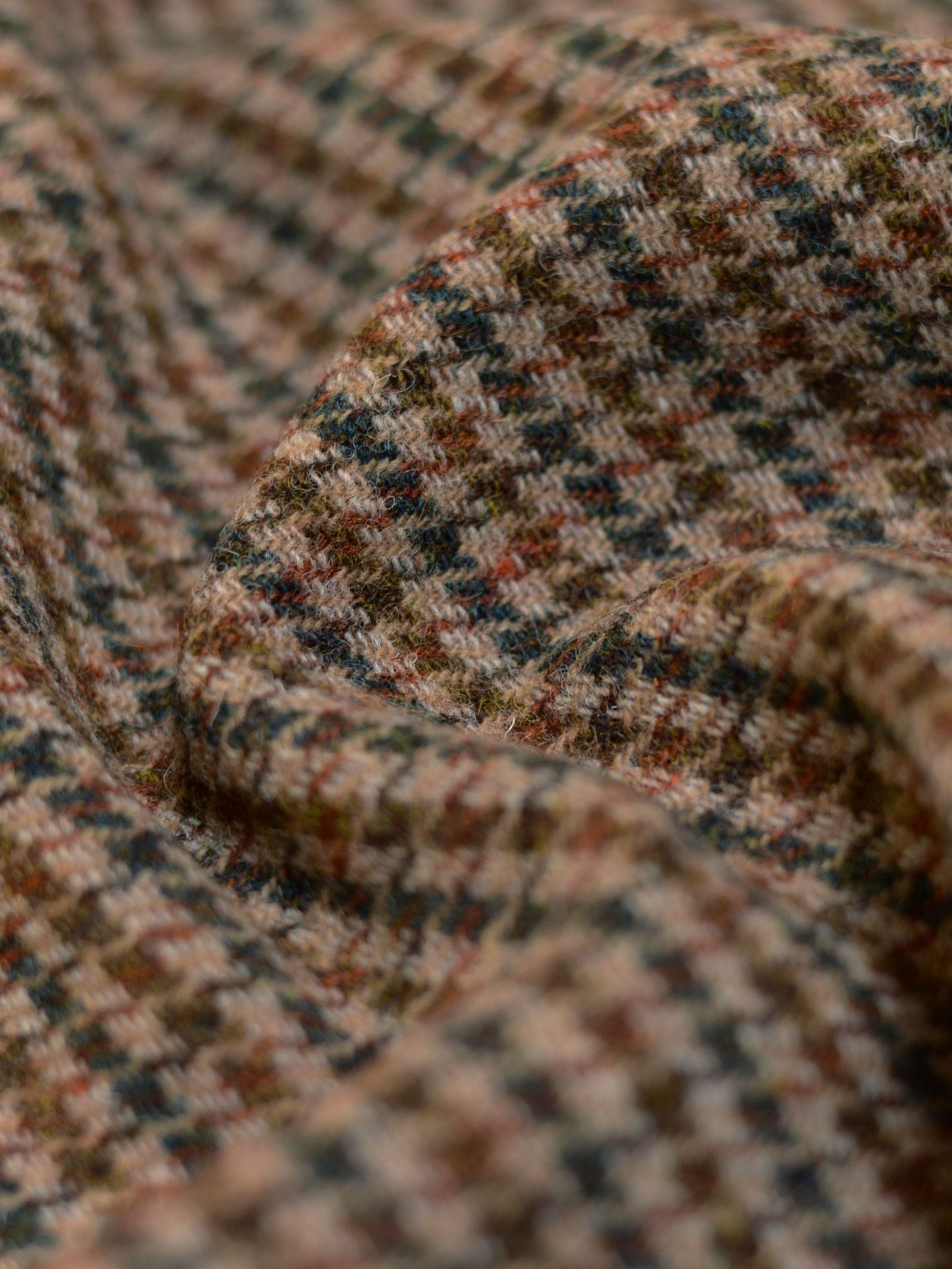 Close-up of Campbell's of Beauly Harris Tweed 93887 fabric, showcasing a small checkered houndstooth pattern in earthy tones with soft folds for depth and texture, evoking classic tweed style.