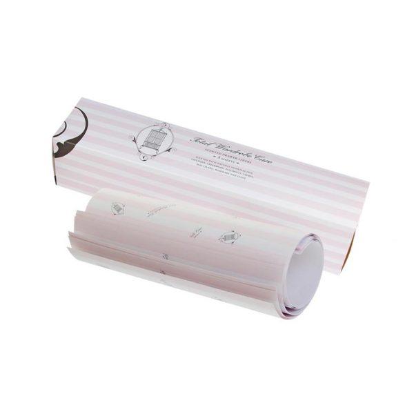 A partially unrolled sheet of Total Wardrobe Care Anti-Moth Drawer Liners with light pink stripes and illustrations, beside its matching box on a white background—ideal for protecting wardrobes and adding elegance to your drawers.