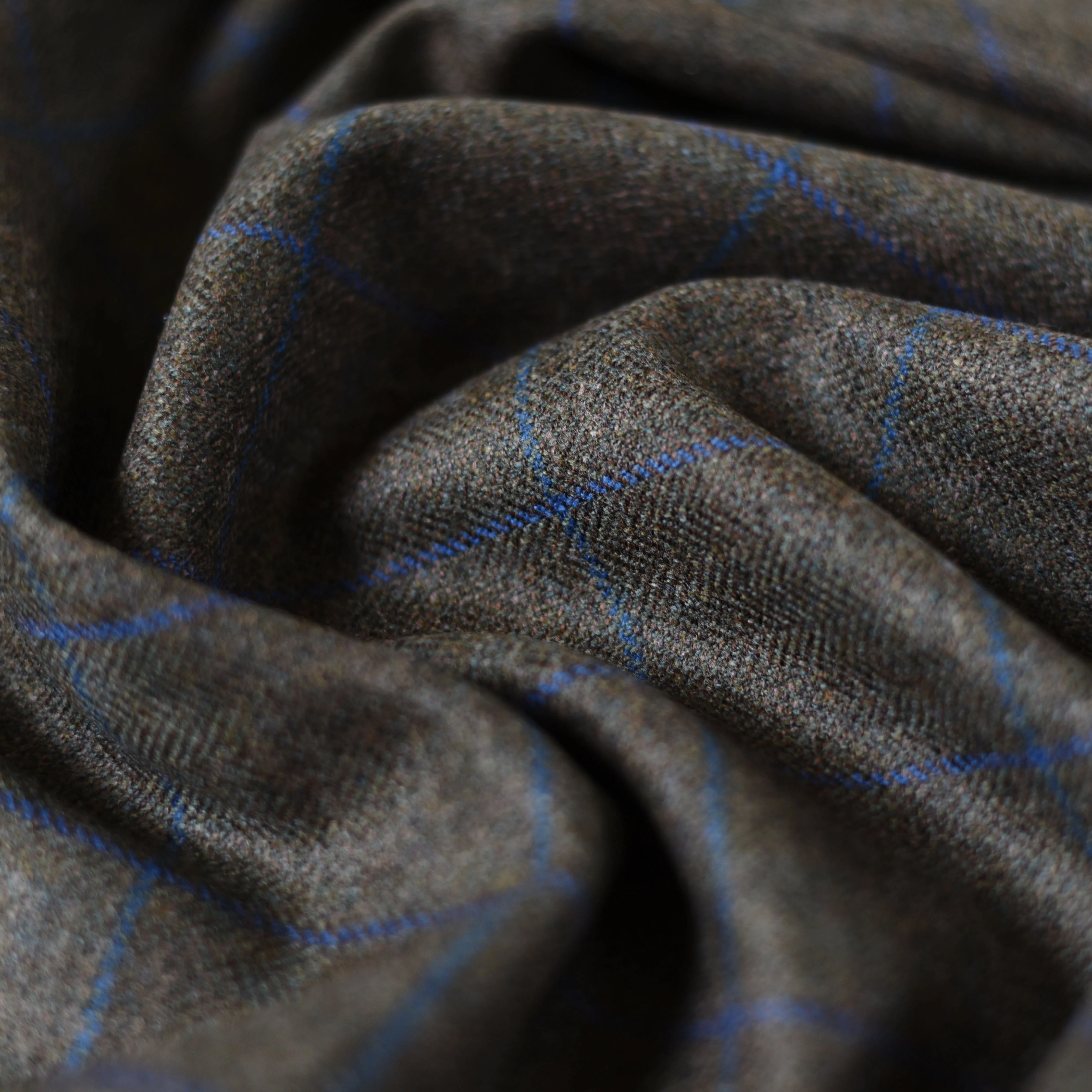 Close-up of House Tweed 61285 by Campbell's of Beauly—brown Scottish tweed fabric with a subtle blue plaid, softly draped to show texture and weave. Ideal for those seeking traditional tweed by the metre.