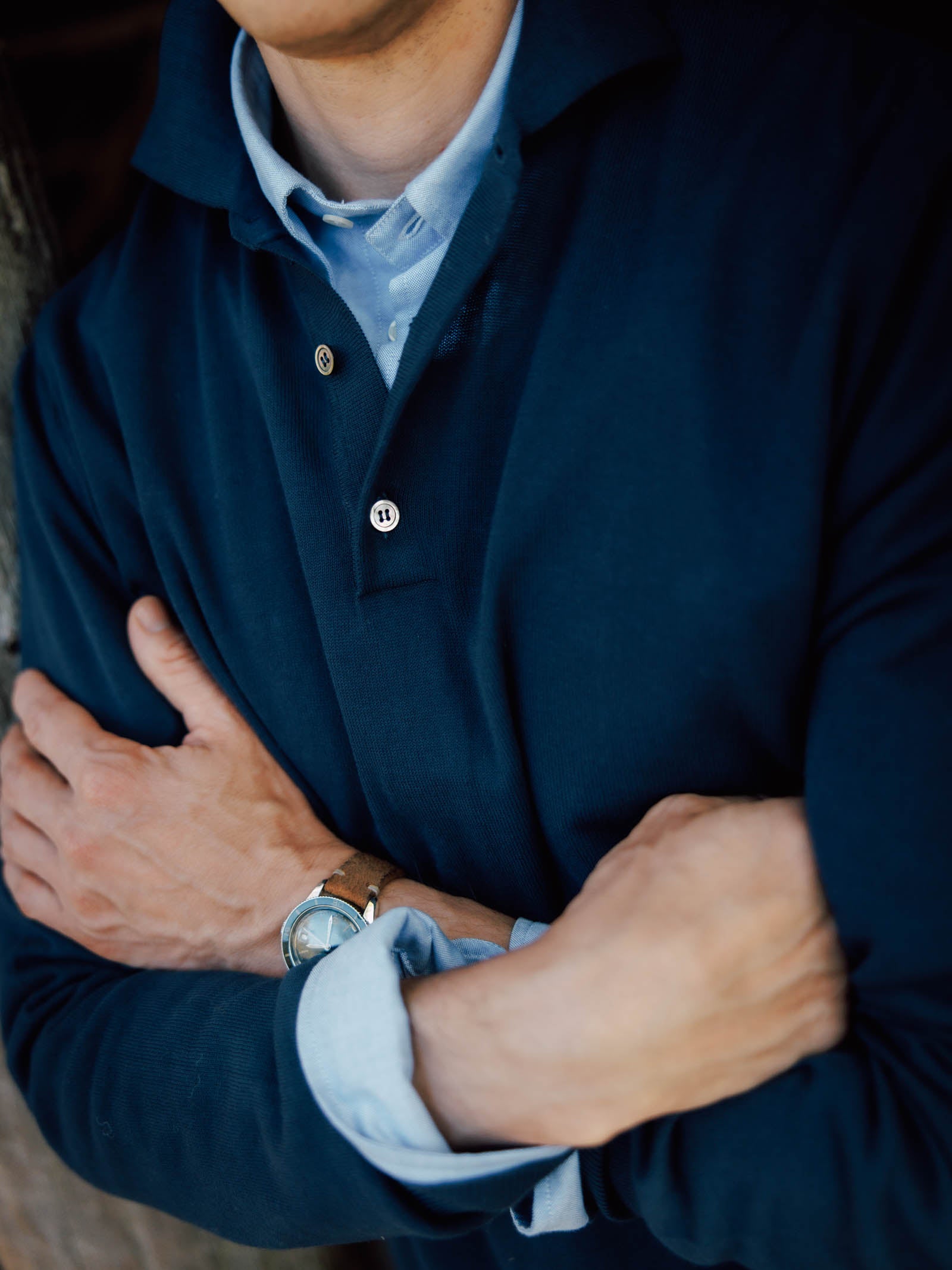 A person with light skin crosses their arms, wearing a Campbell's of Beauly Cotton Rugby in dark blue over a light blue button-down, sporting a silver wristwatch on their left wrist. Their face is partially out of frame.