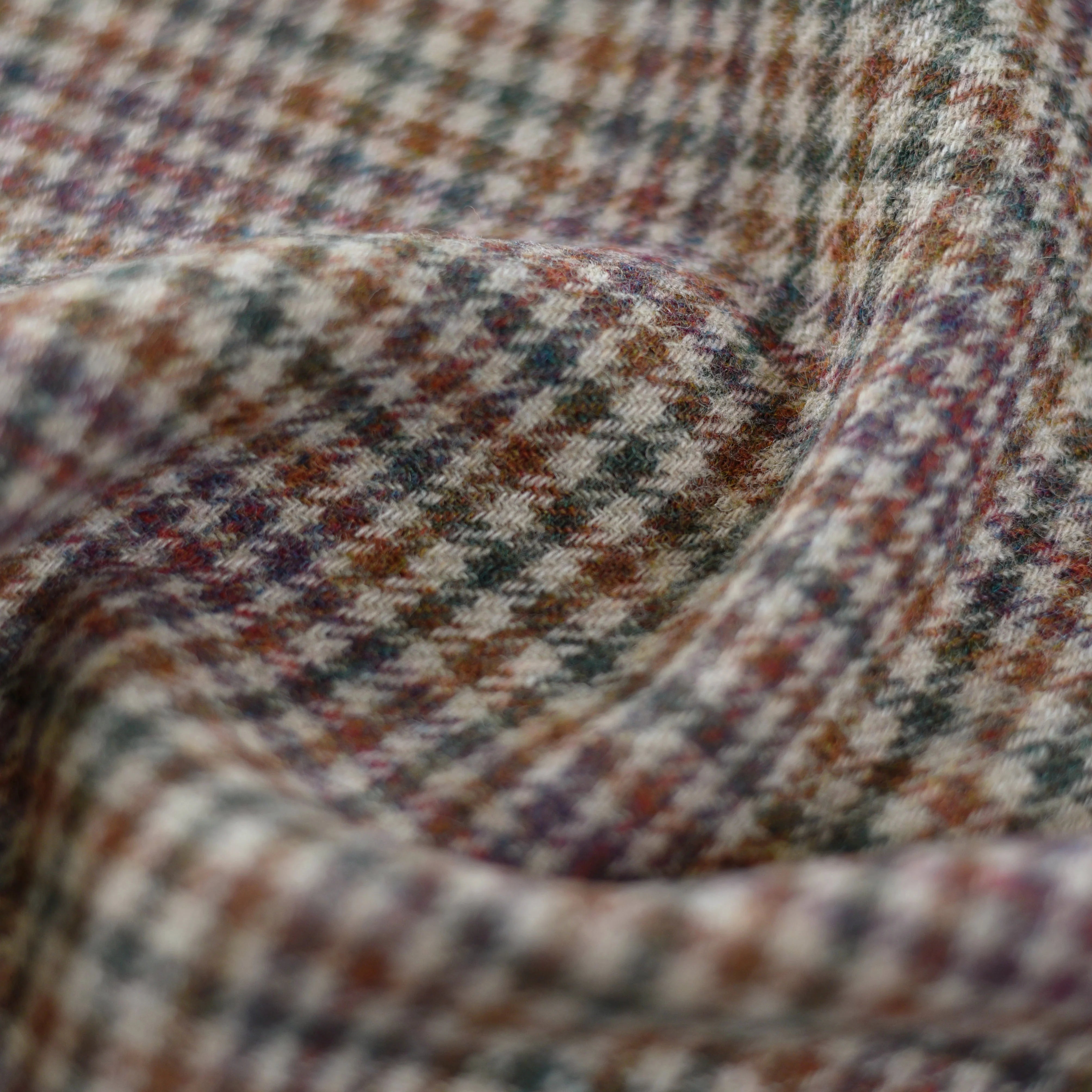 Close-up of Campbell’s of Beauly House Tweed 11054, showcasing its lightweight Shetland wool houndstooth in muted brown, gray, and beige tones. Soft folds and textured weave reflect classic Scottish textile heritage.