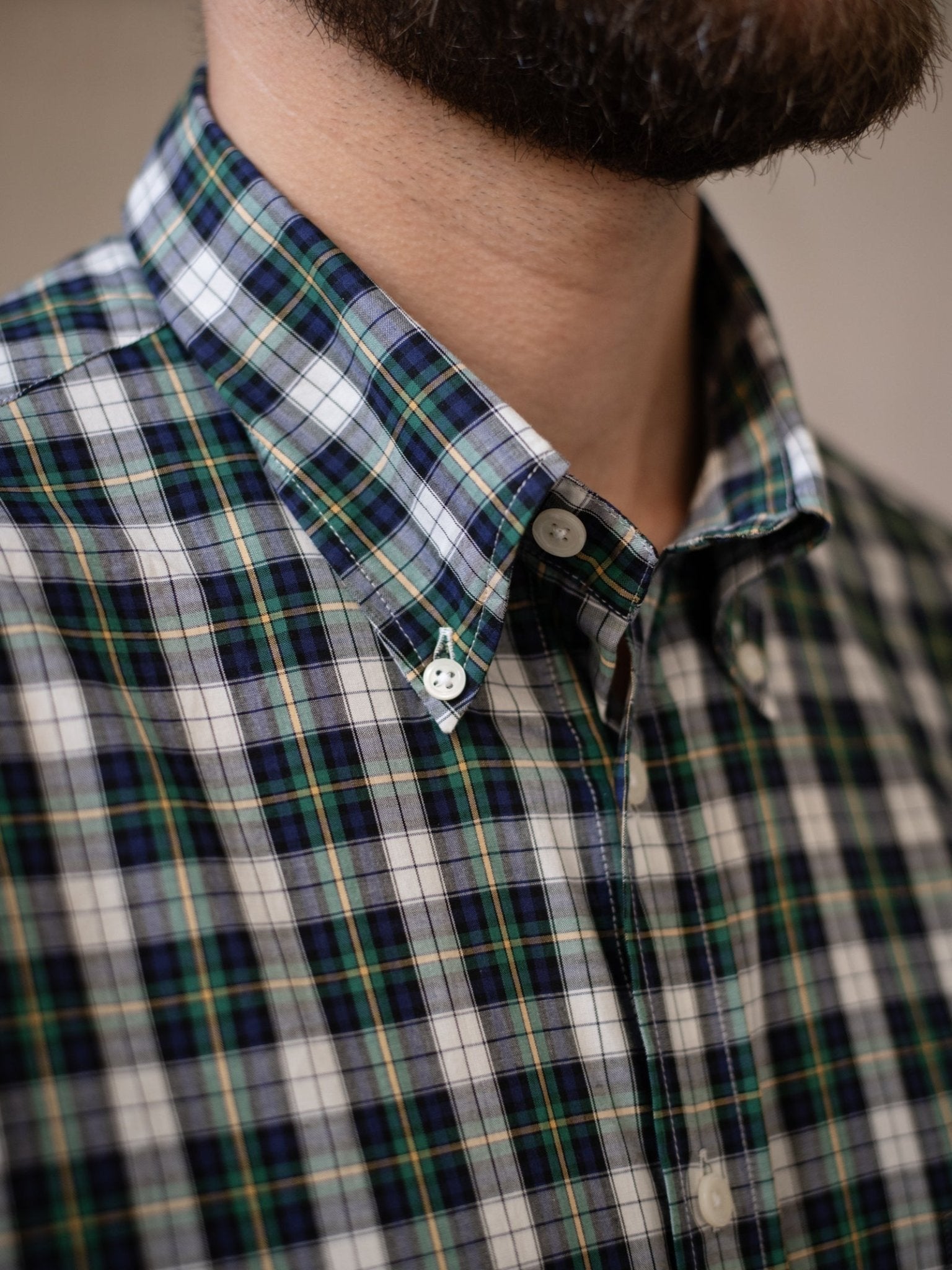 Close-up of a person wearing the Campbell's of Beauly Cotton Tartan Button Down Shirt in a blue, green, white, and yellow Dress Gordon plaid. The shirt collar is buttoned, showing part of the person's beard and neck.