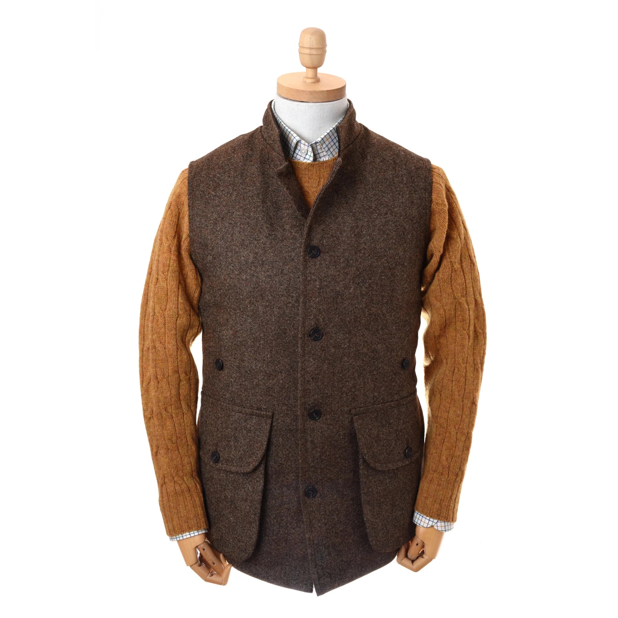 A mannequin models Campbell's of Beauly's Auld Stock Field Nehru Gilet, a brown vest, layered over a mustard cable-knit sweater and checkered dress shirt, with both arms at its sides.