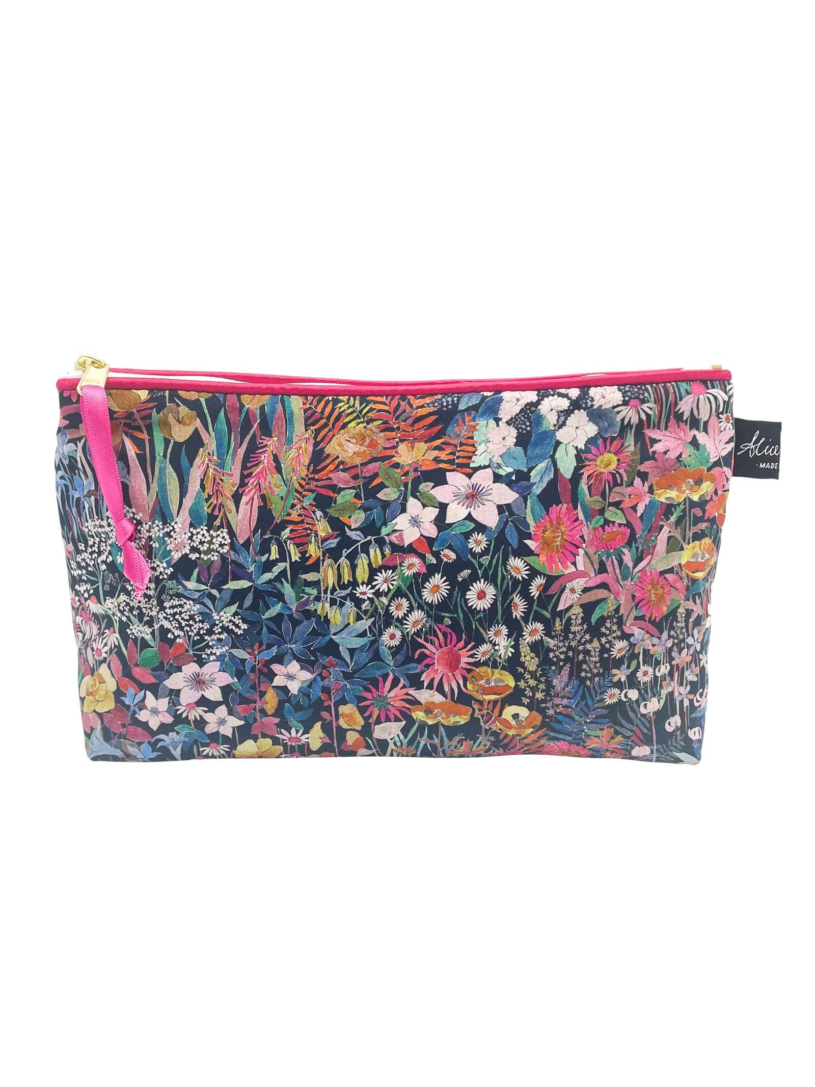 The Alice Caroline Liberty Print Cosmetic Bag features vibrant red, pink, yellow, and green flowers and leaves on a dark background, inspired by Liberty prints. It’s finished with a pink zipper for added style.