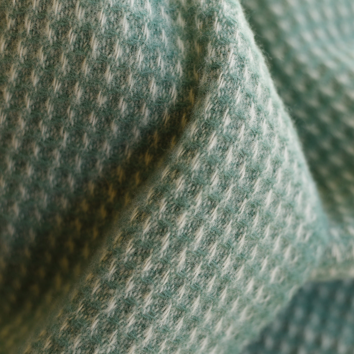 Close-up of the Campbells of Beauly Honeycomb Lambswool Throw, showcasing its soft, textured fabric in a green and white houndstooth pattern with visible honeycomb weave and gentle folds.