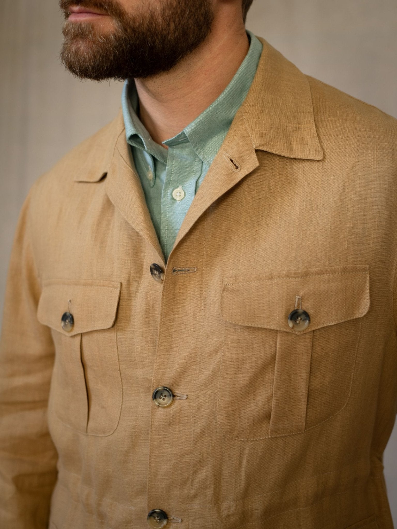 A man with a brown beard wears Campbell's of Beauly Linen Safari Jacket with flap pockets over a mint green shirt. The photo, cropped from the nose down, highlights the jacket’s breathable linen and stylish detailing.