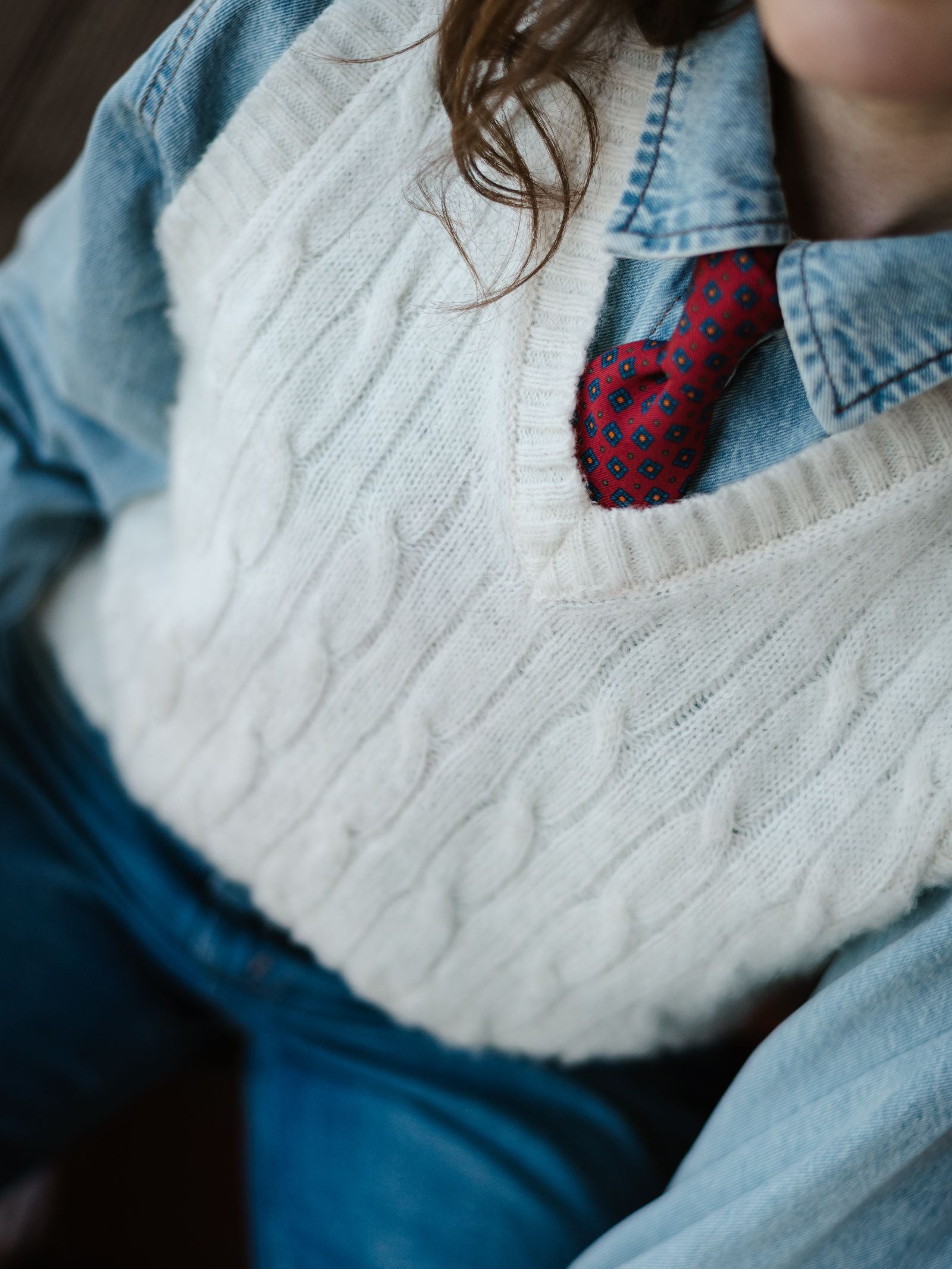 A person wearing a white knitted sweater vest over a denim shirt, accessorized with the Campbell's of Beauly Paisley Silk Tie. Only the upper body is visible.