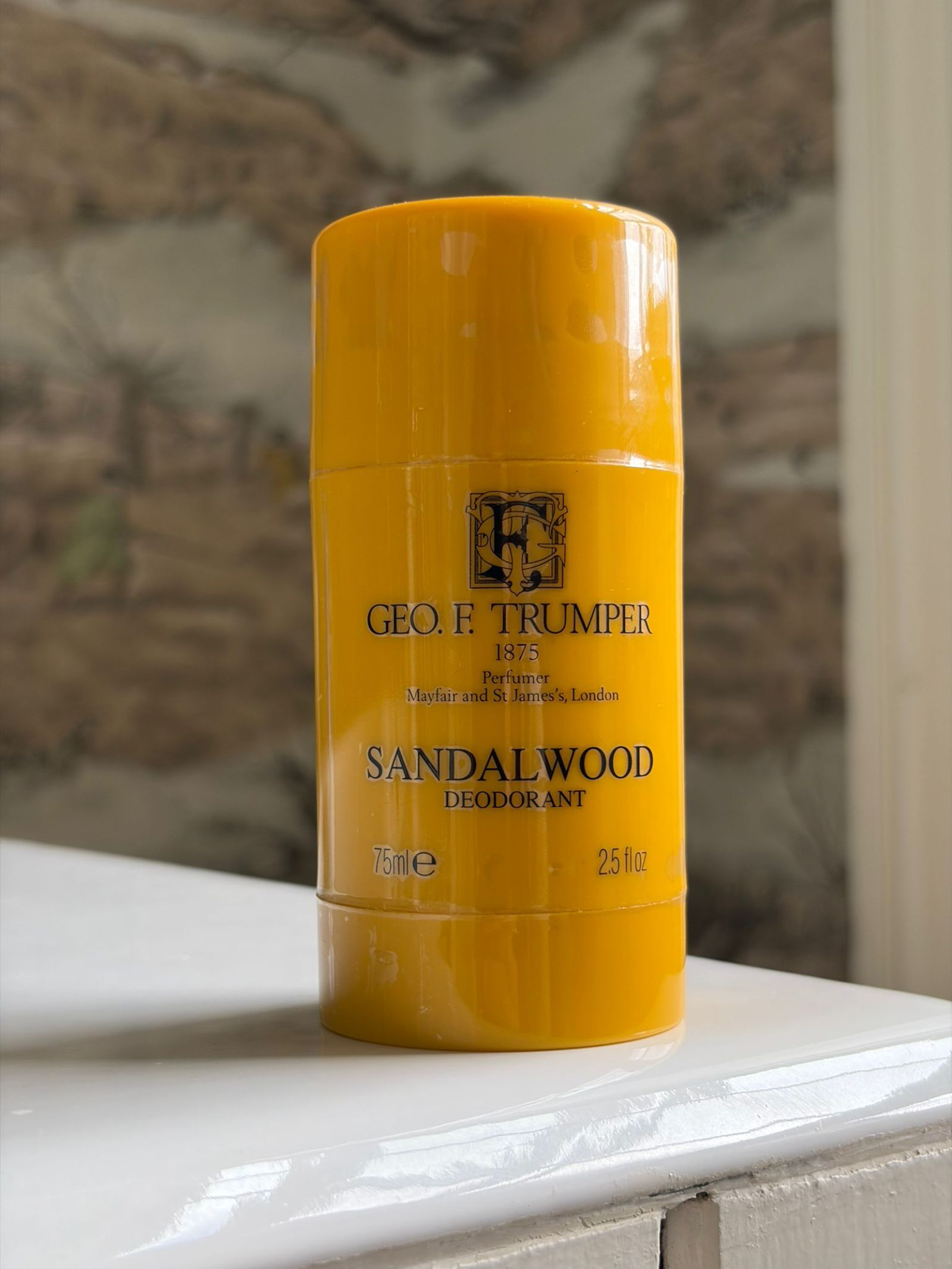 A yellow cylindrical container of Campbell's of Beauly Sandalwood Deodorant Stick (75ml/2.5 fl oz), featuring an alcohol-free formula and long-lasting freshness, sits on a white surface against a blurred, neutral background.