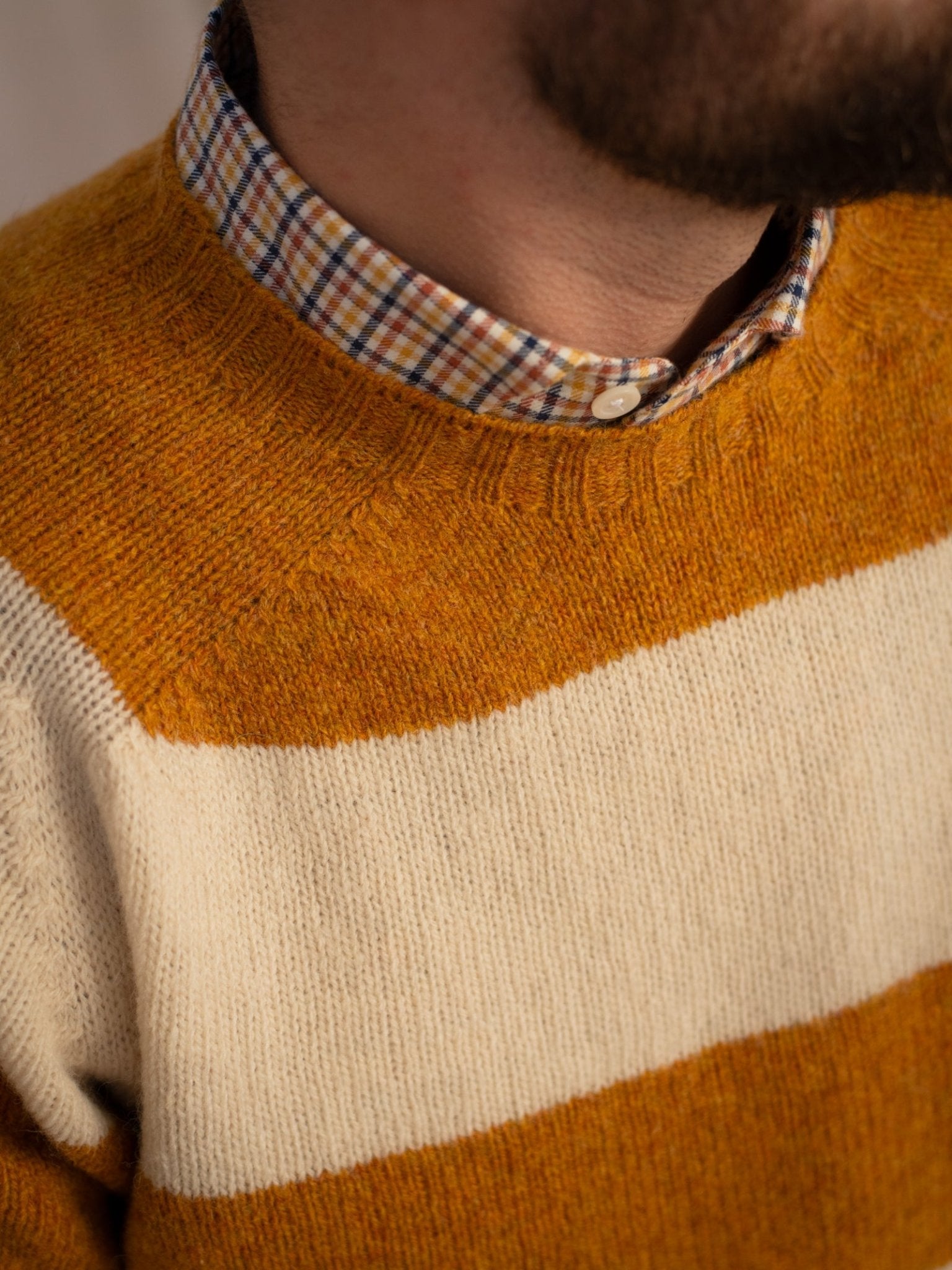 A person wears the Campbell's of Beauly Shetland Stripe Crew Jumper in mustard yellow and white over a plaid shirt, showing only the lower face, neck, and chest—classic Scottish knitwear style.