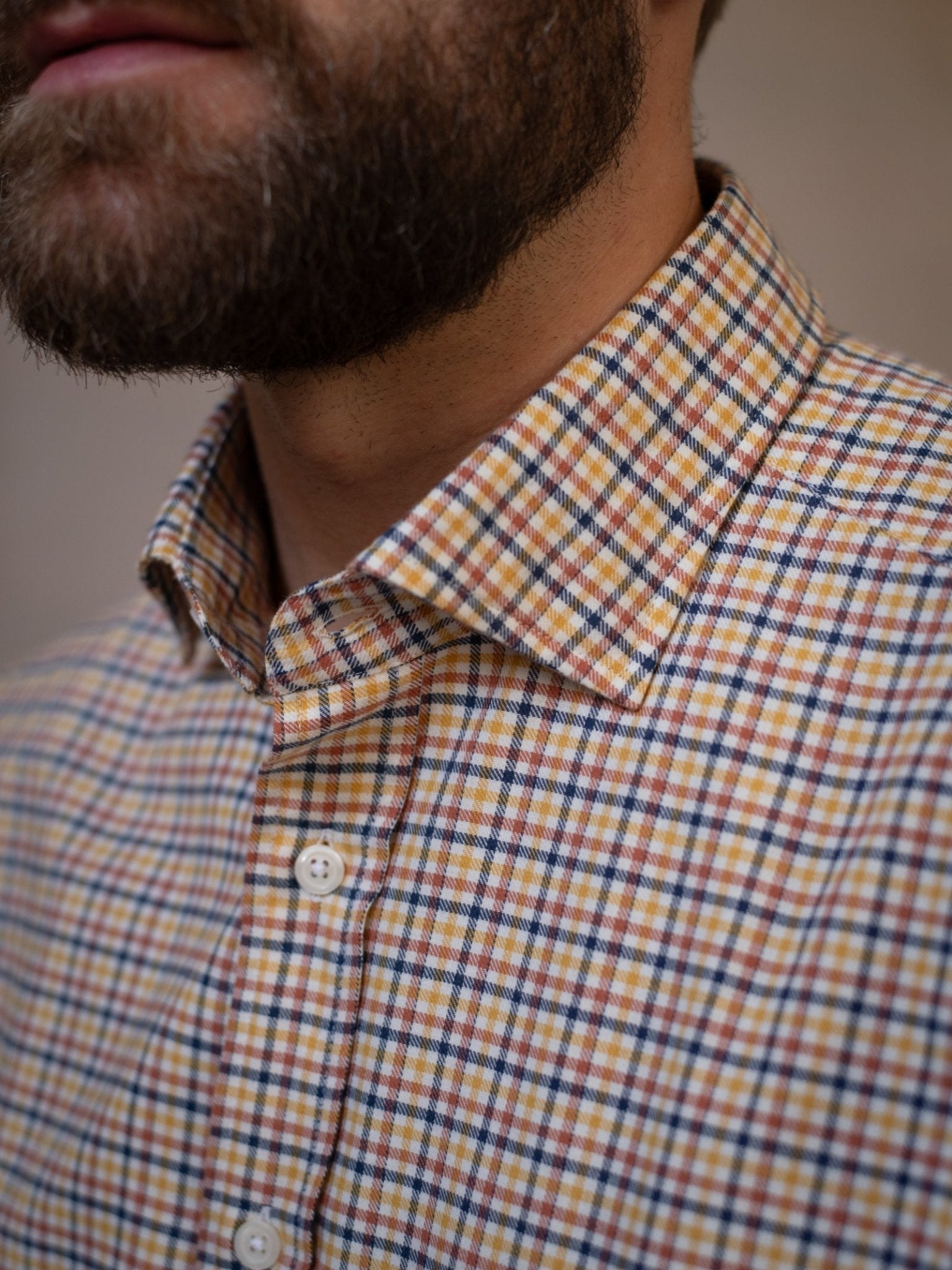 Close-up of a bearded man wearing the Campbell's of Beauly Windowpane Shirt, featuring a yellow, orange, blue, and white plaid pattern. Only his lower face, neck, and upper chest are visible.